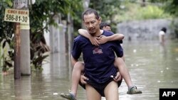 Một người đàn ông Indonesia cõng con trai qua một khu phố bị ngập lụt ở Tangerang trong vùng ngoại ô Jakarta, ngày 27/10/2010