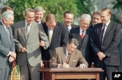 Các nhà lập pháp đứng nhìn Tổng thống Ronald Reagan kí thành luật dự luật cải tổ thuế mang tính dấu mốc trên Bãi cỏ Nam Nhà Trắng, Washington, ngày 22 tháng 10, 1986.