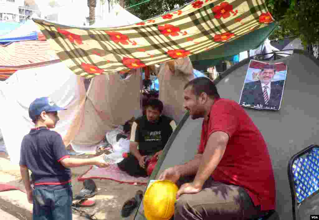 Em bé mang nước cho người của Huynh đệ Hồi Giáo tụ họp bên ngoài đền Rabaa al-Adawiya ở Cairo, 11-7-2013. Ảnh: VOA/Sharon Behn