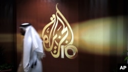 Tư liệu - Một nhân viên người Qatar của kênh tin tức Al Jazeera tiếng Ả-rập đi ngang qua logo của Al Jazeera ở Doha, Qatar.