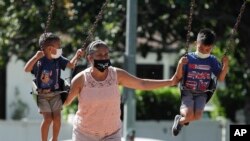 Seorang perempuan dan dua anak-anak mengenakan masker bermain di taman di tengah pandemi virus corona (COVID-19), di Los Angeles, California, 11 Juli 2020. (Foto: AP)