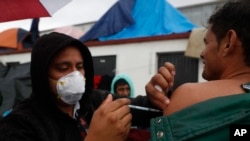 FILE - Mexican Health Ministry representatives give migrants free shots for the flu, hepatitis B, tetanus, and preventible children's diseases at the Barretal shelter for migrants in Tijuana, Mexico, Dec. 6, 2018.