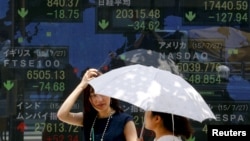 FILE - Women stand in front of a board showing market indices in Tokyo July 28, 2015.